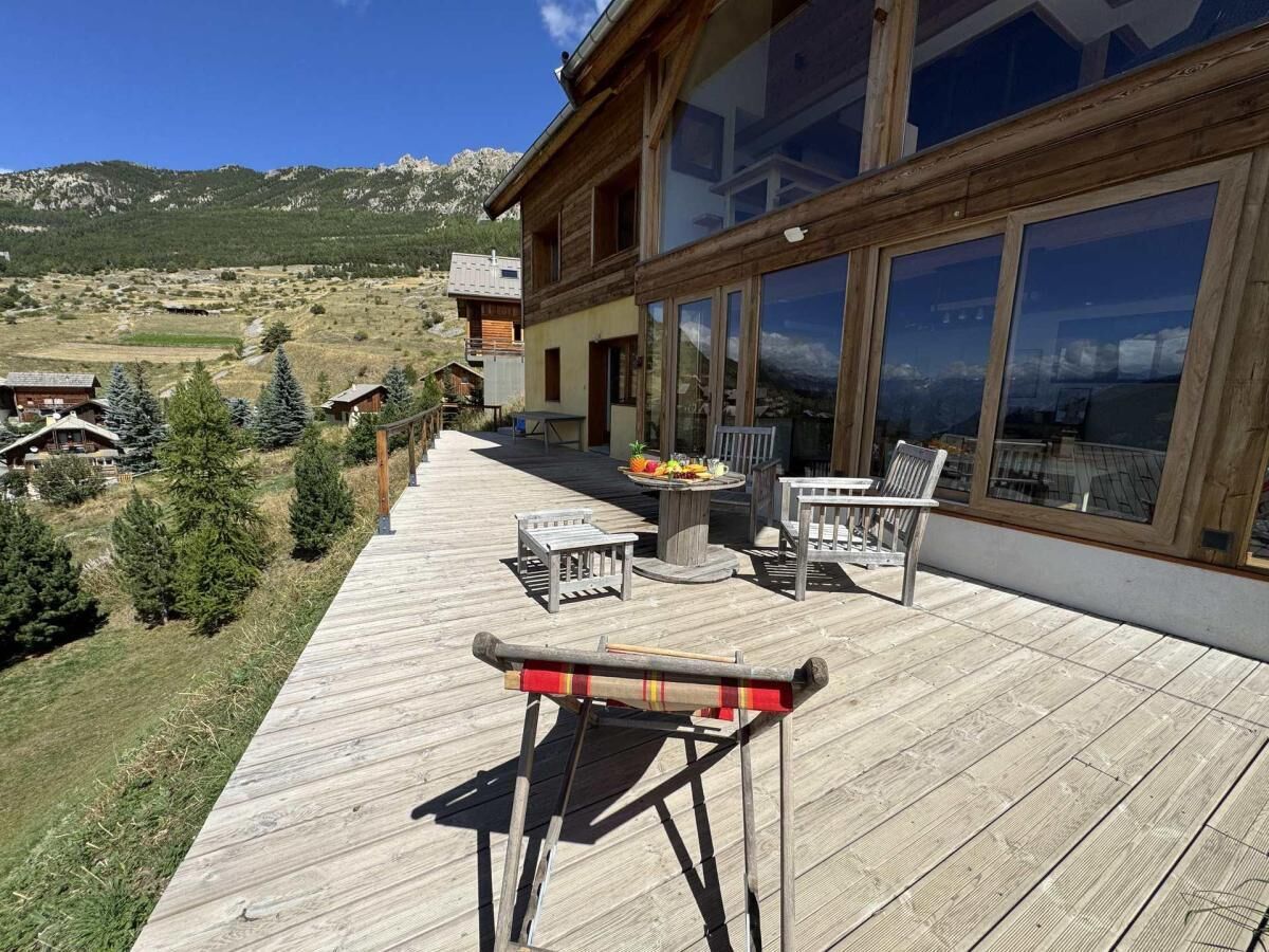 Eine Holzterrasse mit Gartenmöbeln, einer Feuerstelle und Blick auf eine malerische Berglandschaft.