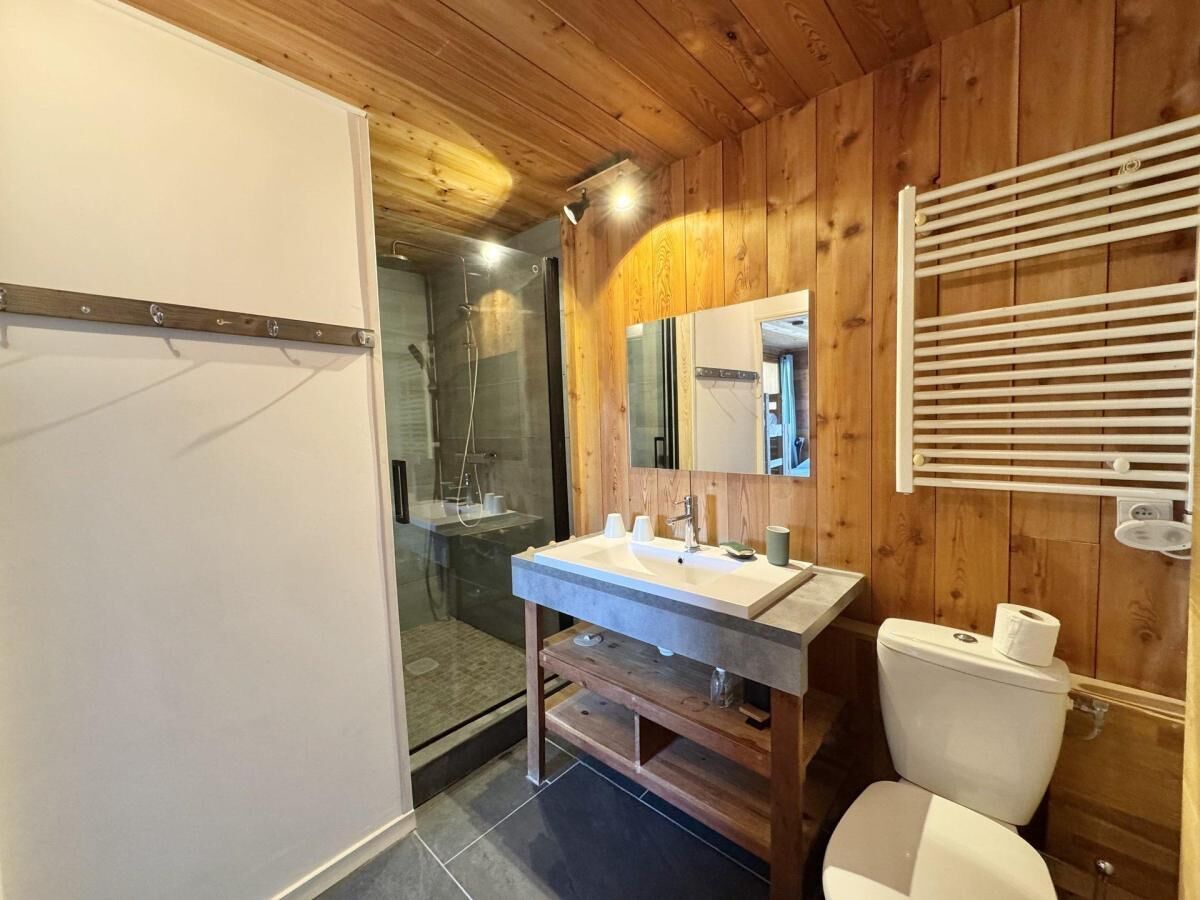 A modern bathroom with a wooden interior, a glass shower enclosure, a double sink vanity, and a toilet.