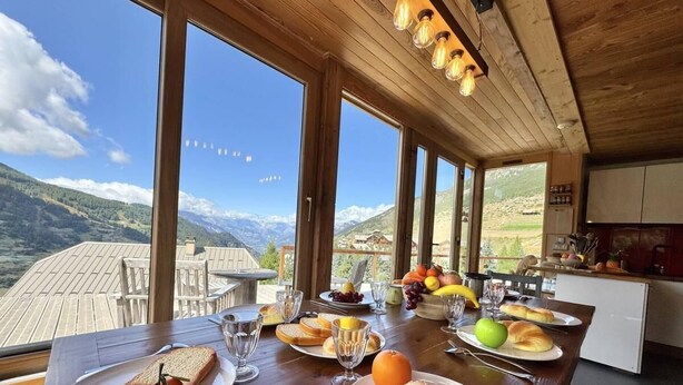 A dining table set with breakfast items, large windows offering mountain views, and a wooden ceiling with hanging lights. - View mountain, terrace, parking, ski locker, 80m², Vars (Vars)