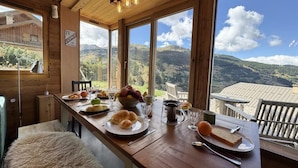 A wooden dining table with breakfast items, large windows with a mountain view, and a sign indicating a license. - View mountain, terrace, parking, ski locker, 80m², Vars (Vars)