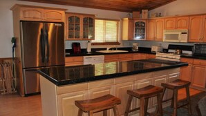 A kitchen with wooden cabinets, a stainless steel refrigerator, a microwave, a stove, and a large island with stools. - Aspen Glen Big Bear Lake (Big Bear Lake)