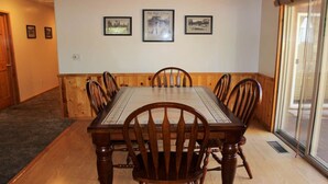 A dining room with a wooden table and chairs, framed pictures on the wall, and a sliding glass door to the right. - Aspen Glen Big Bear Lake (Big Bear Lake)