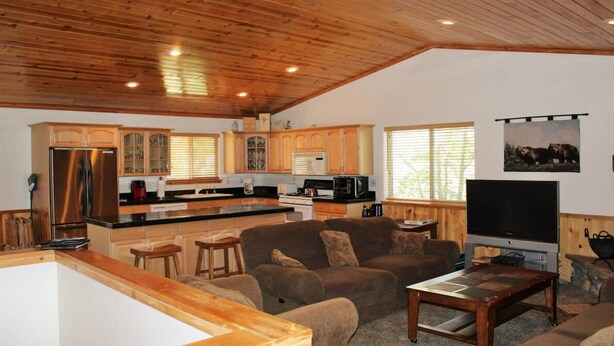 A spacious living area with a wooden ceiling, a kitchen with wooden cabinets, a large flat-screen TV, and a comfortable sofa. - Aspen Glen Big Bear Lake (Big Bear Lake)