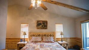A bedroom with a wooden bed, two bedside tables, a ceiling fan, and a painting on the wall. - DeCarlo House Big Bear Lake (Big Bear Lake)