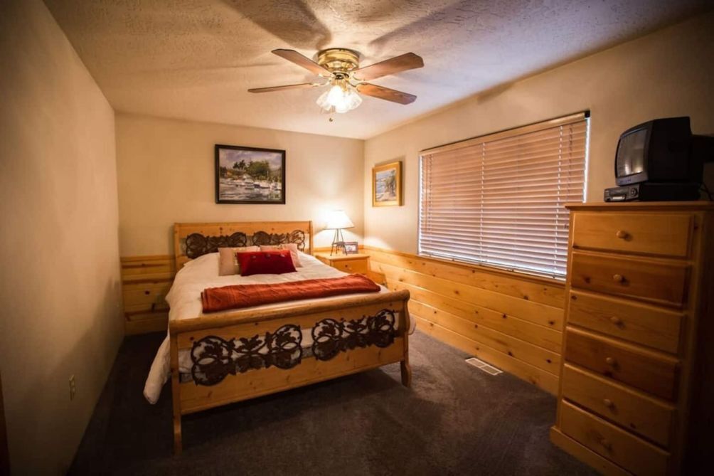 A bedroom with a wooden bed, a ceiling fan, a dresser, and a window with blinds.