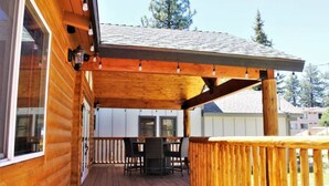 Une terrasse en bois dotée d’un espace salon couvert, d’une balustrade en bois et offrant une vue sur un immeuble d’habitation en arrière-plan.