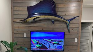 Un salón con una pared de madera, una escultura de pez montada, un televisor, una planta y un sofá blanco.