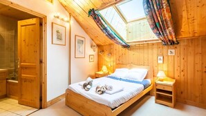 Et hyggeligt soveværelse med træloft, ovenlysvindue, seng med hvide sengetøj og et lille natbord med en lampe.