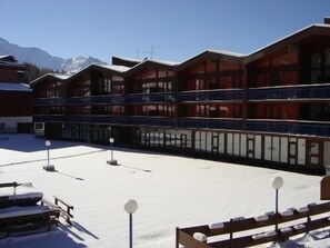 Ein Hotel mit mehreren Balkonen, einem mit Schnee bedeckten Innenhof und einer Bergkulisse.