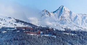Une montagne enneigée, avec un sommet bien visible, et une zone de villégiature comprenant des bâtiments et des arbres.