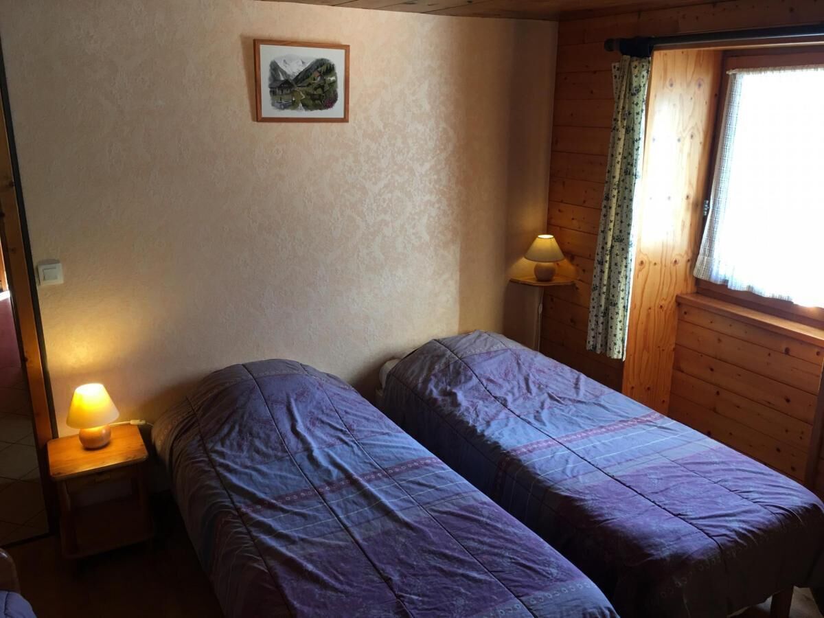 A room with two beds, a nightstand with a lamp, a wooden dresser, a window with curtains, and a framed picture on the wall.