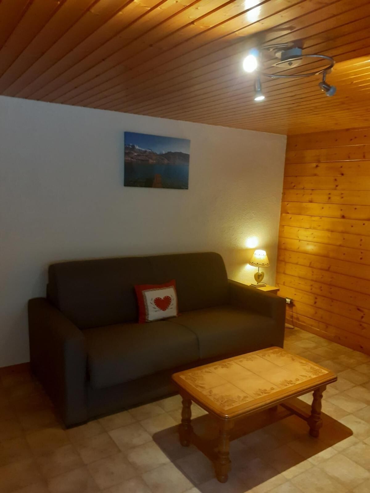 A cozy living room with a dark sofa, a wooden coffee table, a wall-mounted picture, and a lamp.