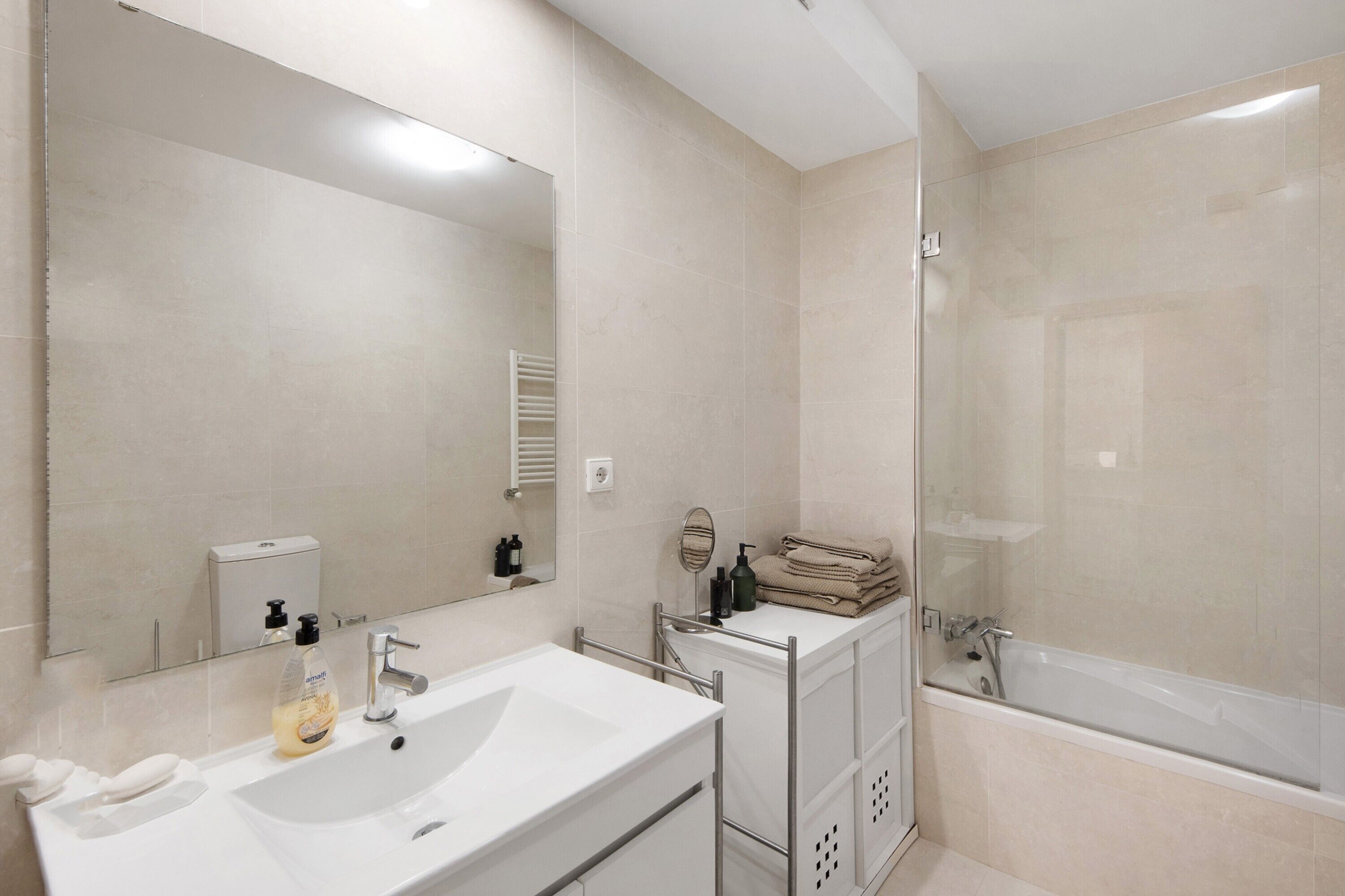 Een moderne badkamer met een grote spiegel, een witte wastafel en een douche met glazen wanden.
