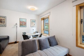 Ein modernes Wohnzimmer mit einer Couch, einem Esstisch mit Stühlen, einer Lampe und gerahmten Bildern an der Wand.
