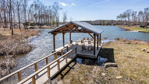 A wooden dock leading to a covered seating area with chairs and tables by a river.