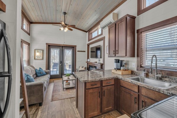 A spacious kitchen with wooden cabinets, a granite countertop, and a built-in oven. There is a large window with blinds, a ceiling fan, and a sink with a faucet.