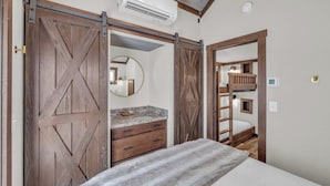 A bedroom with a bed, a dresser, and a mirror. There is a sliding barn door and a bunk bed in the adjacent room.