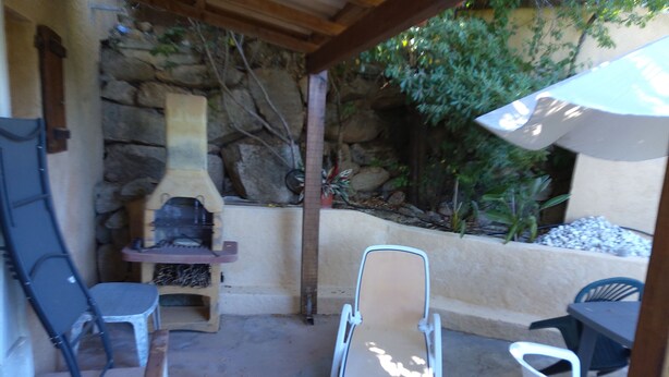 An outdoor patio with a stone wall, a barbecue grill, and a seating area with chairs and a table. - Seaside vacations (Coti-Chiavari)