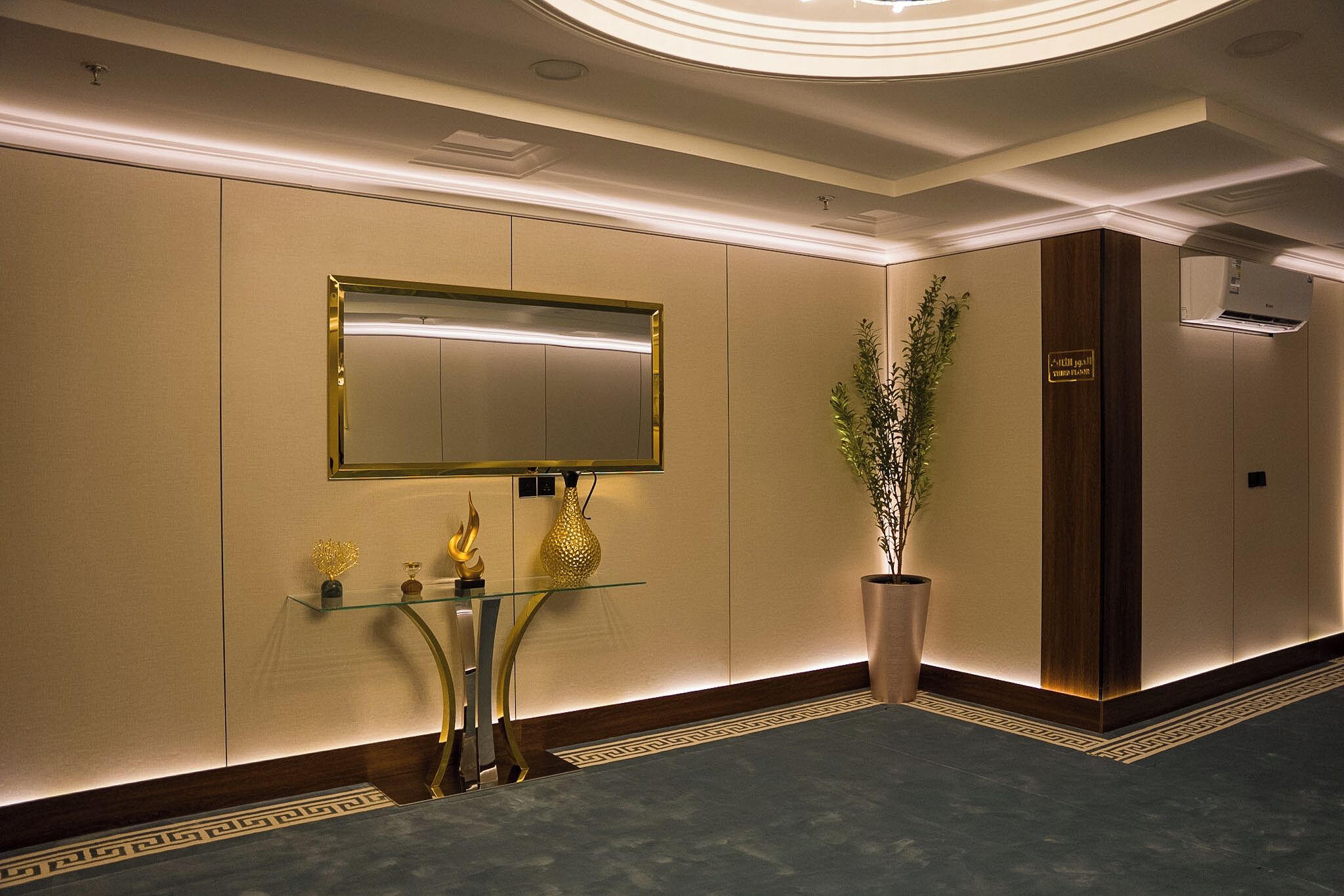 A modern hotel lobby with a large mirror, a reception desk, a potted plant, and a wall-mounted air conditioning unit.