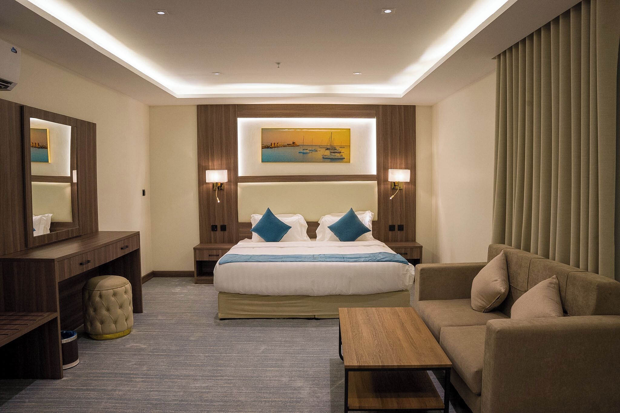 A hotel room with a large bed, a sofa, a desk, and a painting on the wall.