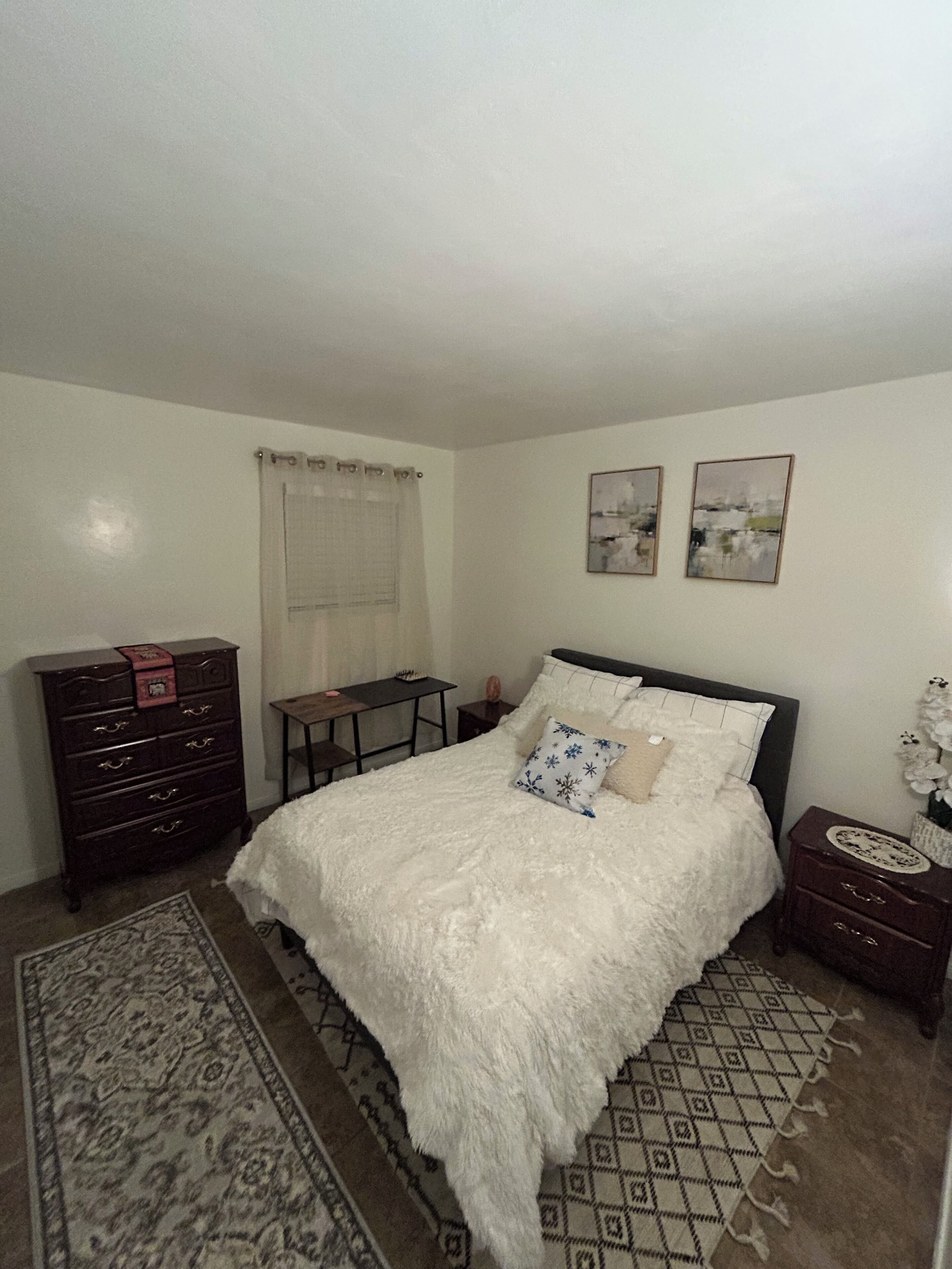 Quarto com uma cama grande, penteadeira, mesa de cabeceira, escrivaninha e janela com cortina.