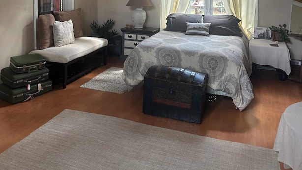 Une chambre avec un grand lit, un bureau, une chaise, une fenêtre avec des rideaux, un ventilateur de plafond et une carte accrochée au mur.
