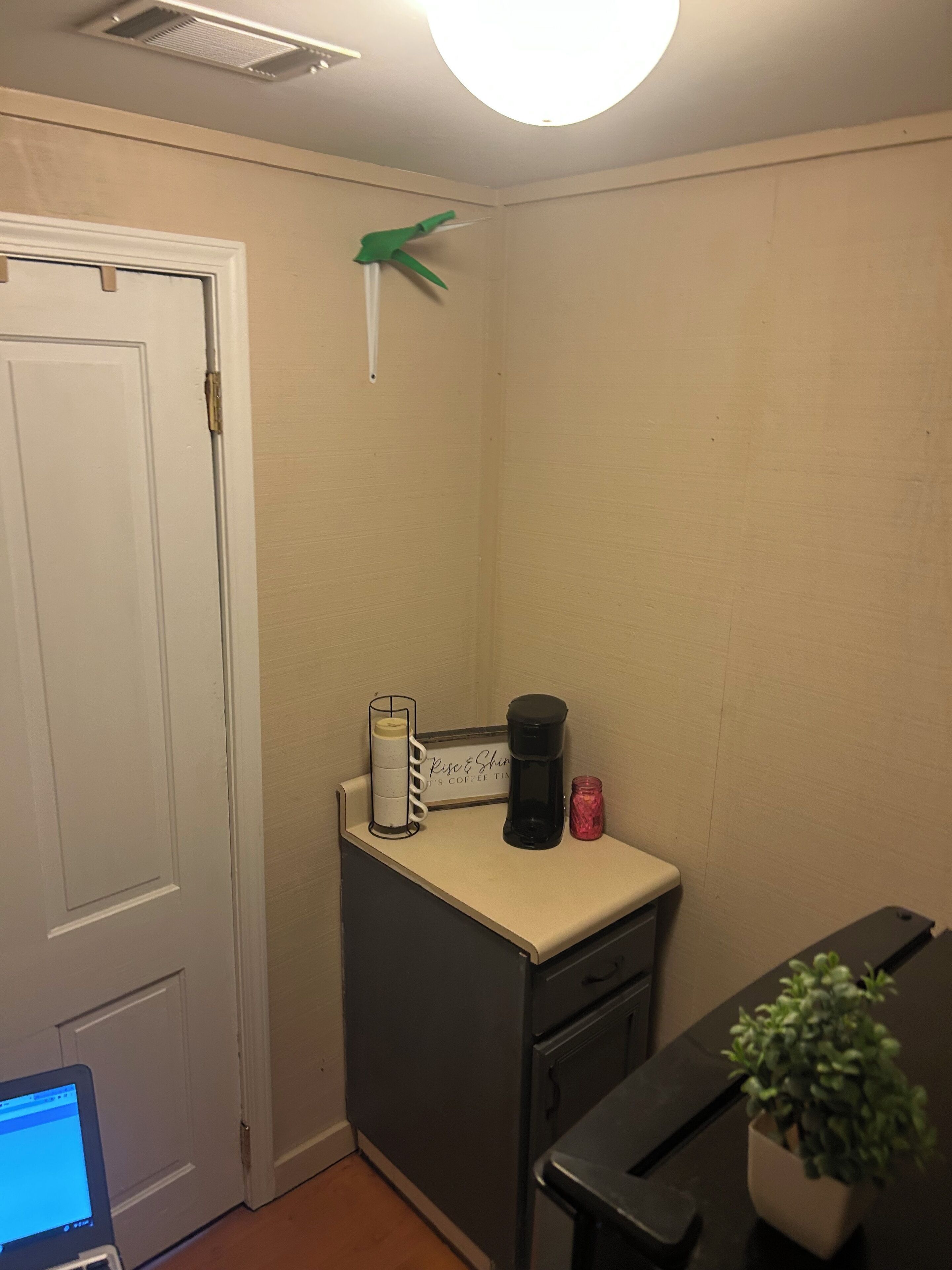 A small kitchenette with a coffee maker, a candle, and a sign that says "Rise & Shine It's Coffee Time".