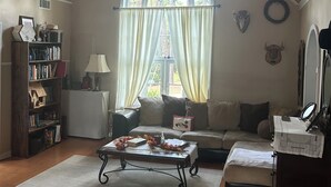 Un salon chaleureux avec un haut plafond en bois, une grande fenêtre en arc de cercle, une bibliothèque, un canapé, une table basse et un miroir.