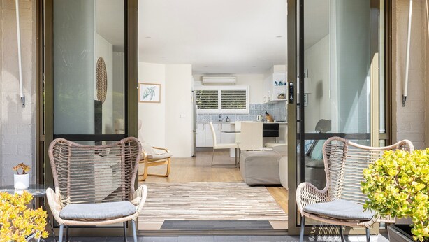 Eine moderne Wohnung mit Glastür, Korbstühlen, einem Essbereich und einer durch die Tür einsehbaren Küche.