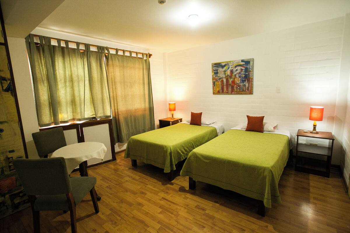 A room with two single beds, a small table, a chair, and a desk.
