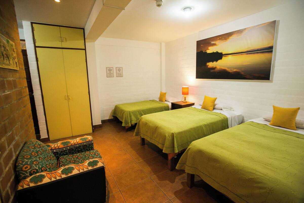 A hotel room with two beds, a sofa, a desk, and a painting of a sunset.