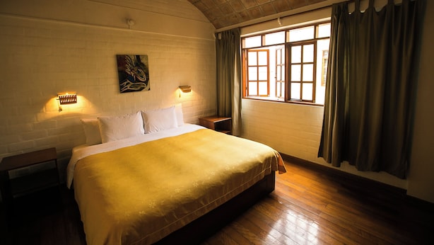 A bedroom with a large bed, two bedside lamps, a window with curtains, and a brick wall. - Casa de Baraybar (Lima)