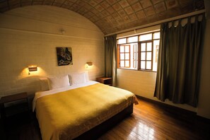 A bedroom with a large bed, two bedside lamps, a window with curtains, and a brick wall. - Casa de Baraybar (Lima)