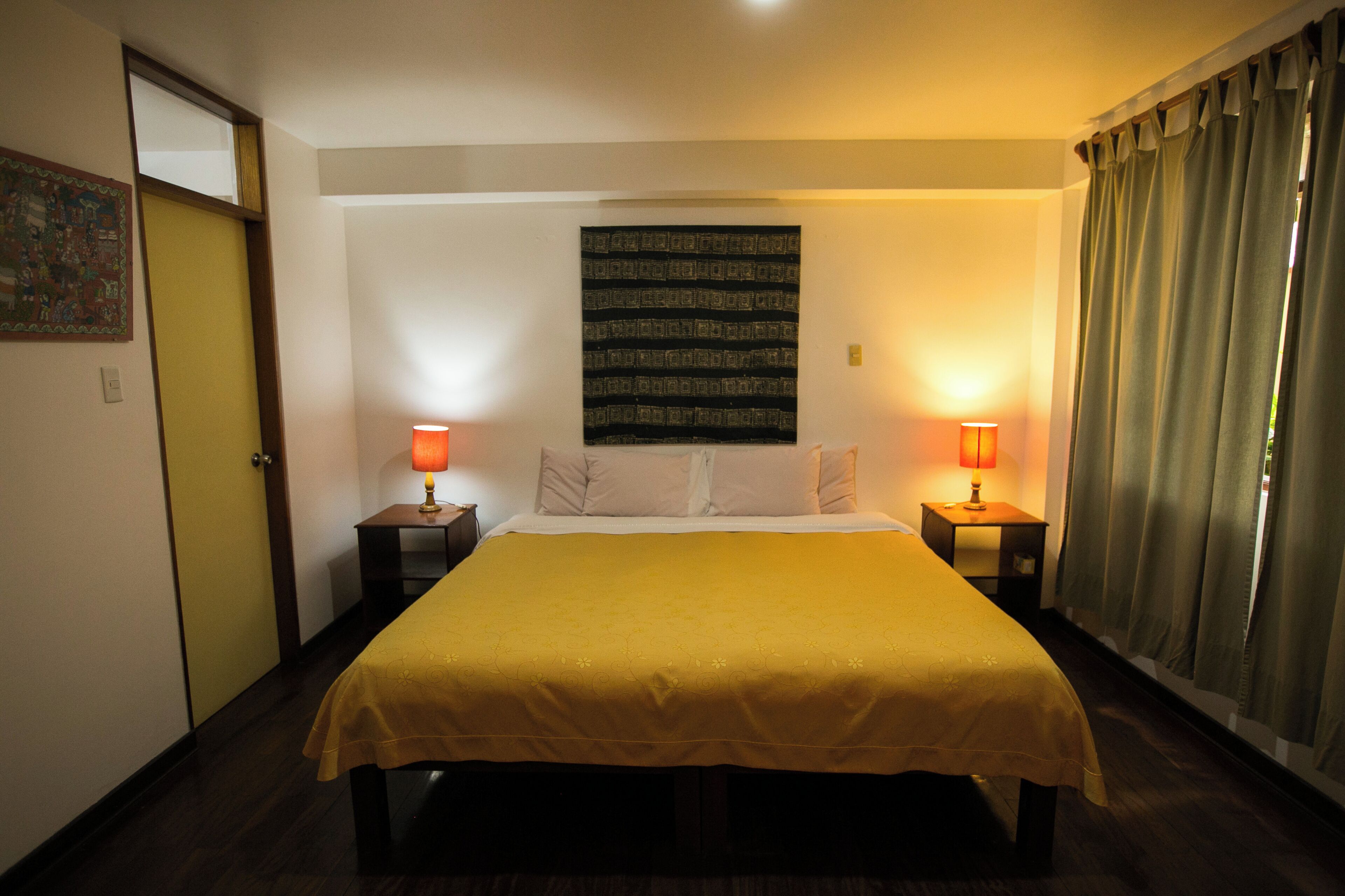 Une chambre d’hôtel avec un grand lit, deux tables de chevet avec des lampes, une tapisserie murale et une porte.