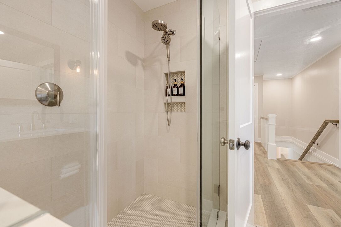 Un bagno moderno con doccia vetrata, parete rivestita in piastrelle bianche e pavimento in legno.