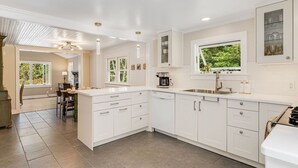 Une cuisine moderne avec des meubles blancs, un grand îlot central et une fenêtre donnant sur un espace verdoyant.
