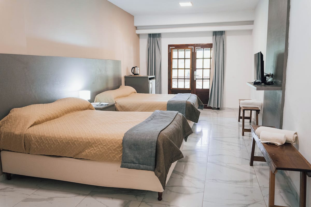 Habitación de hotel con dos camas, un escritorio, una silla, un televisor y una ventana con cortinas.