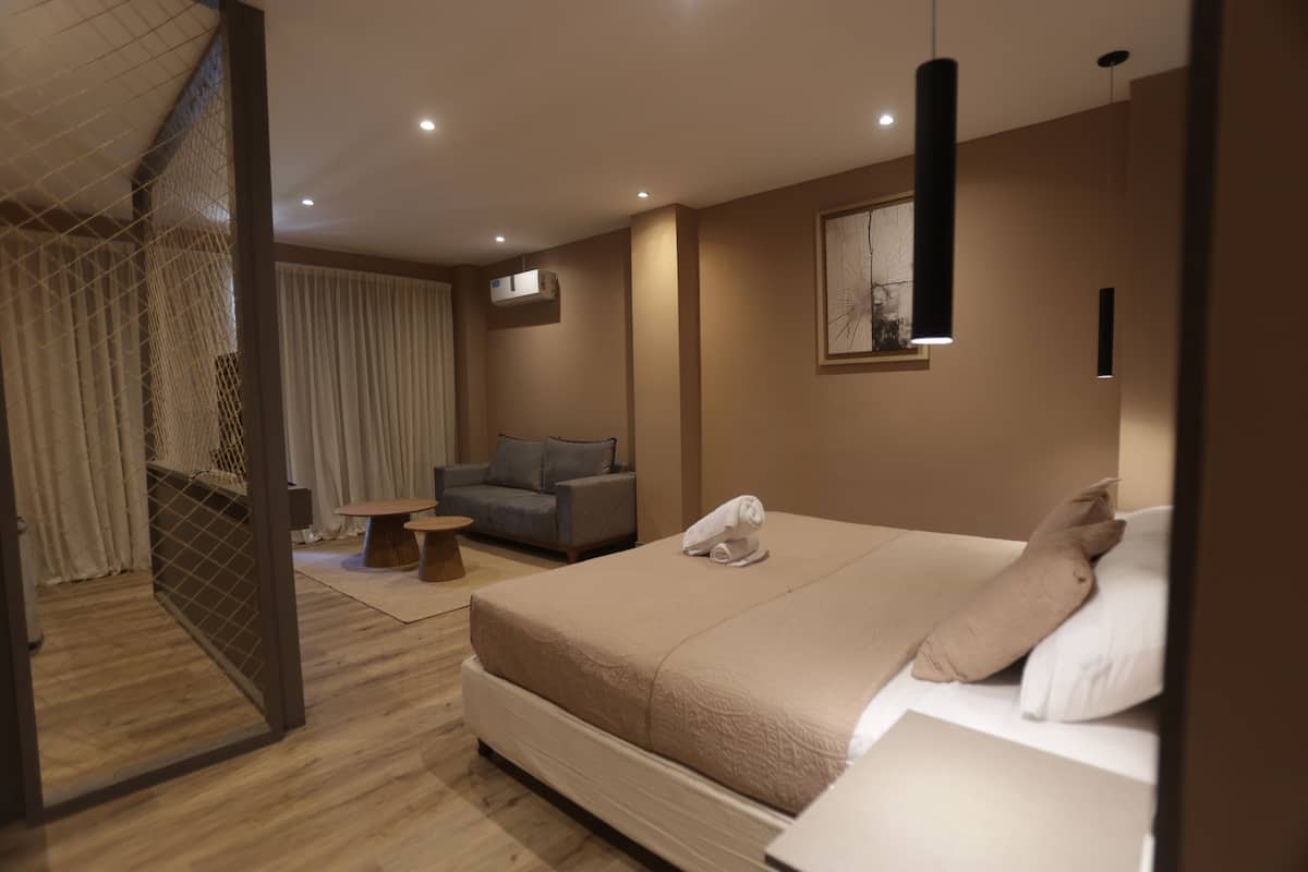 Una habitación de hotel moderna con una cama grande, un sofá, una mesita pequeña y un televisor en la pared.