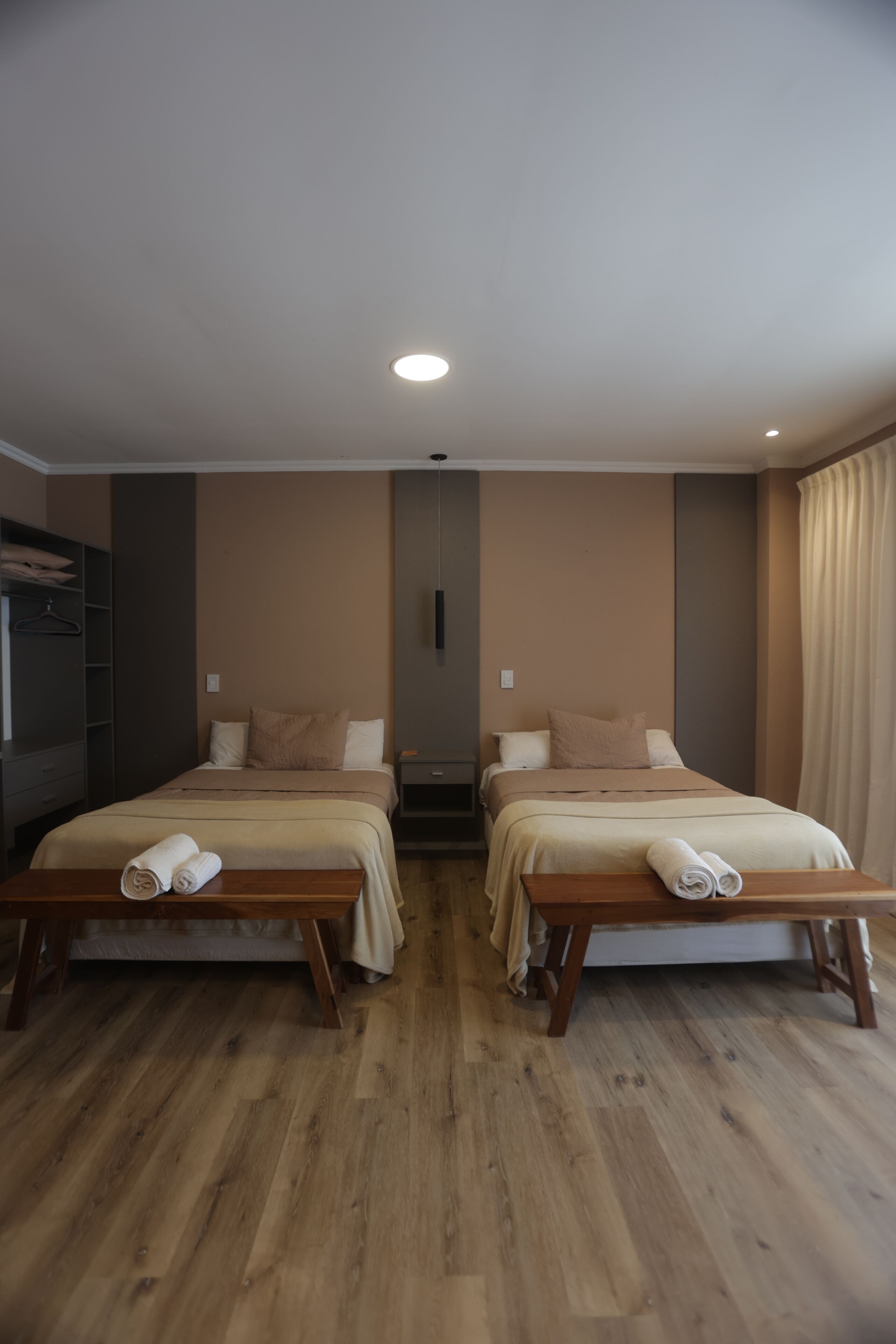 A hotel room with two beds, a wooden bench, a wardrobe, and a television.