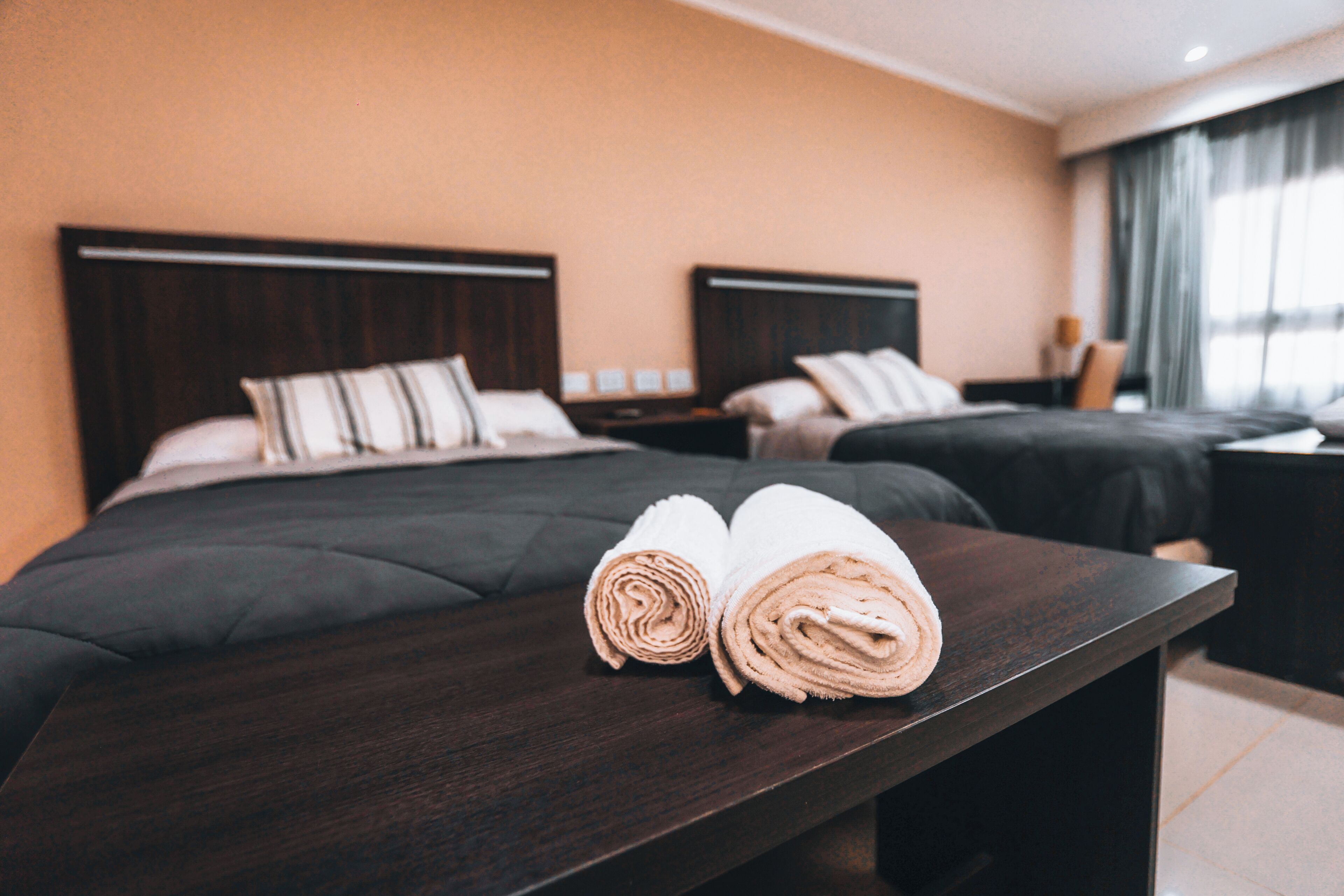 Ein Hotelzimmer mit zwei Betten, dunklen Holzkopfteilen und einem Nachttisch aus Holz mit einer Lampe.