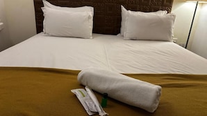 Una habitación de hotel con cama, dos almohadas, una toalla enrollada y una botella de loción.