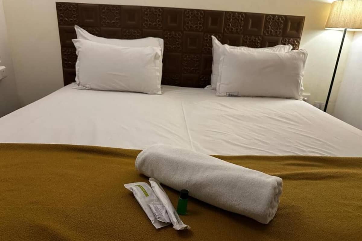 Une chambre d’hôtel avec un lit, deux oreillers, une serviette enroulée et une bouteille de lotion.