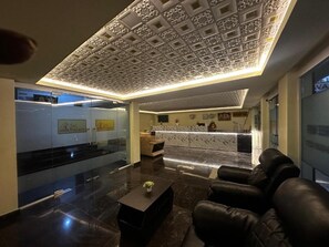 Un vestíbulo moderno con mostrador de recepción, asientos de cuero y un techo decorativo.