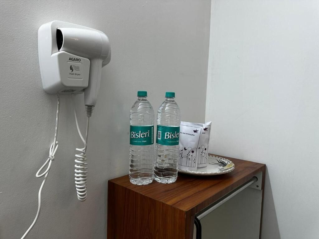 A hairdryer mounted on a wall, two Bisleri water bottles, and a plate with a packet on a wooden table.