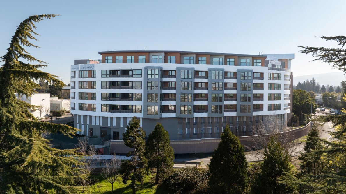 Een hotel met meerdere verdiepingen, modern vormgegeven, met een combinatie van glazen en bakstenen gevels, en omgeven door bomen.