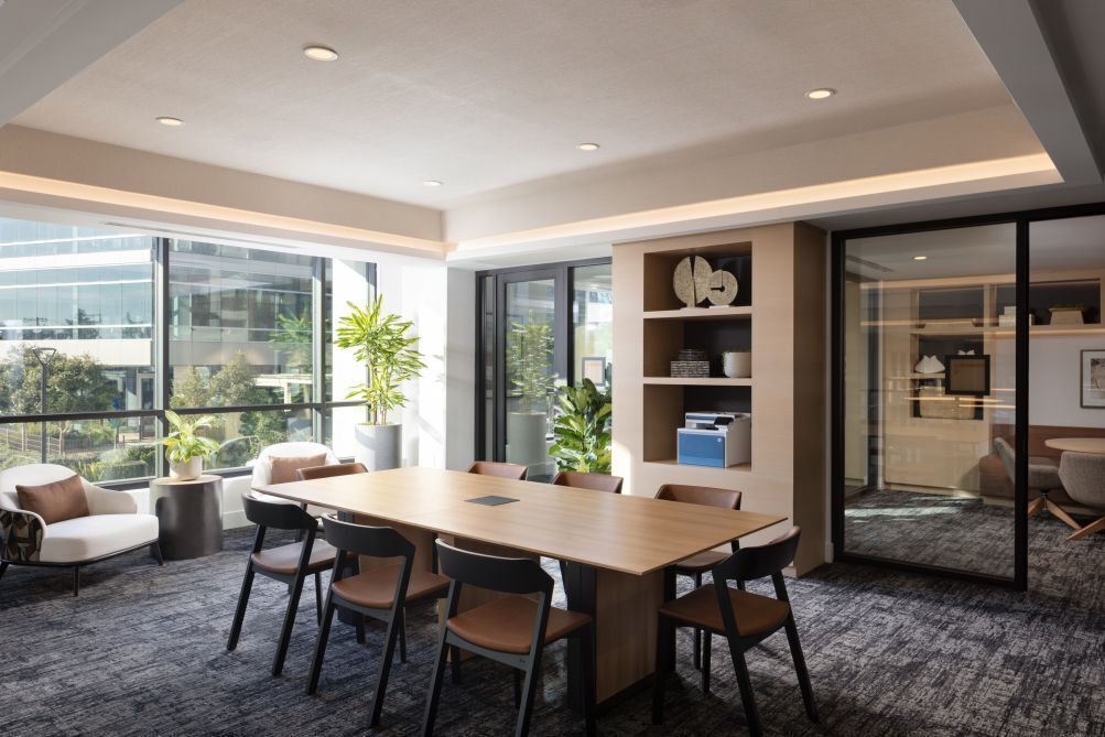 A modern meeting room with a large table, chairs, a bookshelf, and a glass partition.