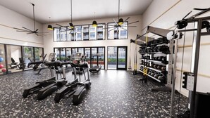 Un gimnasio moderno con cintas de correr, bicicletas estáticas y máquinas de pesas. Cuenta con ventanas amplias, ventiladores de techo y un soporte para pesas.