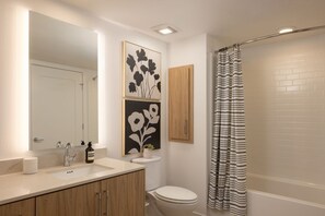 Een moderne badkamer met een witte wastafel, houten kastjes, een toilet en een douche met een gestreepte gordijn.