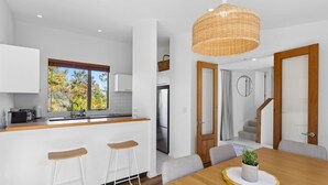 A modern kitchen with a large window, a dining area with a wooden table, and a staircase leading to another level. - Birdsong House, a contemporary family home close to the beach. (Kaiteriteri)