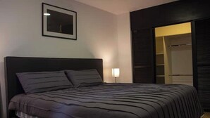 A bedroom with a large bed, a bedside table, a framed picture on the wall, and a closet with sliding doors. - Sabana Sur House (San José)